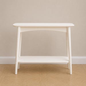 May include: A white console table featuring a rectangular top with rounded corners, four tapered legs, and a lower shelf. The structure is made of smooth, solid material with a clean finish, providing a stable surface and an open storage area.