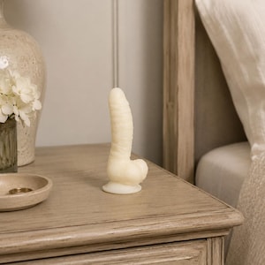 May include: A phallic-shaped object with a textured, off-white surface and a rounded base. The item features a cylindrical body with horizontal ridges and a bulbous, rounded end, standing upright on a flat surface.