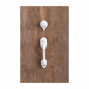 May include: Two white cabinet hardware pieces are shown against a brown wooden background. The top piece is a knob, and the bottom piece is a pull with a decorative design. The hardware is likely for a cabinet or drawer.