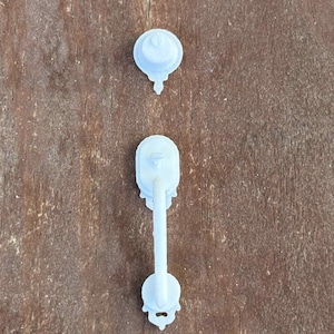 May include: Two light blue cabinet knobs and pulls are displayed against a brown wooden surface. The knobs are round with a small decorative element on top. The pull has a long, straight handle with decorative ends.