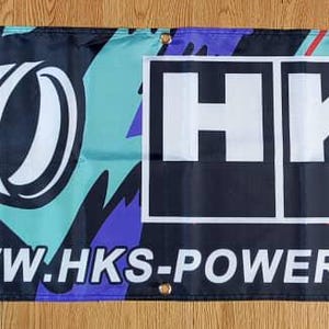 May include: A black and white banner with a blue, purple, and green abstract design. The banner features the HKS logo and the text "www.hks-power.co.jp".