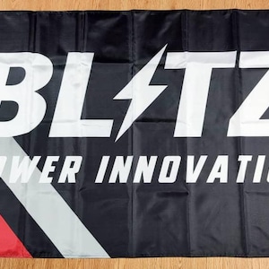 May include: Black and white flag with the text "BLITZ POWER INNOVATION" in white letters on a black background. The flag has a diagonal red and gray stripe.