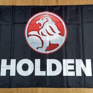 Könnte beinhalten: Eine schwarze Flagge mit einem weißen Holden-Logo. Das Logo zeigt einen roten Kreis mit einem weißen Löwen darin. Der Löwe blickt nach rechts und hat eine rote Mähne.