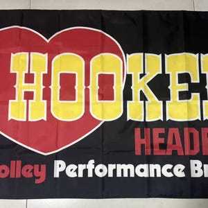 May include: Black flag with the words "HOOKER HEADERS" in yellow and red, with a heart-shaped logo. The text "A Holley Performance Brand" is also displayed in white.