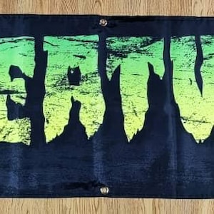 Op de afbeelding: Een zwarte banner met het woord "CREATURE" in groene en gele letters met een verweerde, versleten uitstraling.