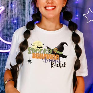 Puede incluir: Camiseta blanca con un diseño de Halloween. El diseño incluye una luna llena, un sombrero de bruja, una araña y el texto "Spooky Behavior Analyst Rachel" en verde, naranja y negro. Una prenda casual para el día a día.