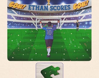 May include: A jigsaw puzzle featuring a soccer stadium scene with a player wearing a blue jersey with the name ETHAN and number 10 on the back. The text GOAL! ETHAN SCORES GOAL! appears above the stadium, with a trophy and confetti visible.