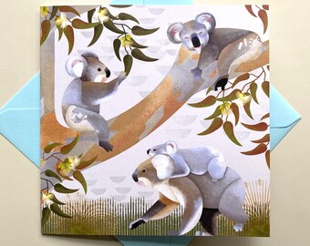 May include: A greeting card featuring a whimsical illustration of three koalas on a eucalyptus tree branch. The koalas are depicted in a cartoon style with soft, gray fur and large, black eyes. The background is a light gray with a pattern of small, white circles. The card is perfect for sending a sweet and heartwarming message.