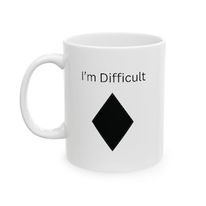 May include: White ceramic mug with the text "I'm Difficult" above a black diamond symbol. The mug has a curved handle and a glossy finish. The design is simple and bold, making a statement.