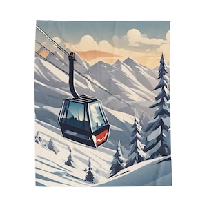 Può includere: Una coperta con un'illustrazione stilizzata di una funivia che sale su una montagna innevata. La cabina è nera con un dettaglio rosso, sullo sfondo di cime innevate e un cielo pastello. La coperta è un elemento d'arredo per la casa a tema invernale.