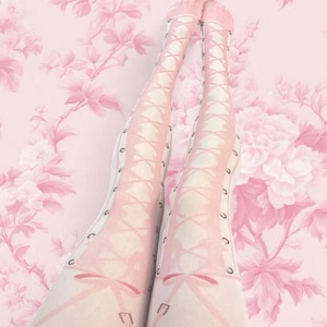 May include: Sheer light pink tights featuring a printed design of a corset-style lace-up pattern running down the front of each leg. The graphic includes dark eyelets and crisscrossing ribbons that mimic the appearance of a laced boot or bodice.