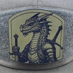 May include: A green and brown baseball cap with a black and white embroidered patch of a dragon wearing armor and holding a sword. The patch is on the front of the cap.
