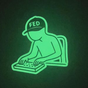 May include: A glowing green sticker featuring a person seated at a keyboard. The person is wearing a cap with the letters "FED" on it. The sticker has a black background.