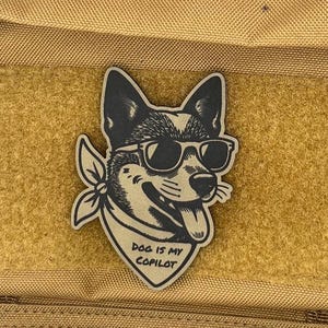 May include: A tan tactical bag with a patch featuring a dog wearing sunglasses and a bandana. The patch reads "DOG IS MY COPILOT". The bag has multiple pockets and zippers.