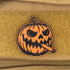 May include: A tan tactical vest with a patch featuring an orange jack-o'-lantern smoking a cigar. The patch is affixed to a tan velcro square on the vest. The pumpkin has a menacing expression.