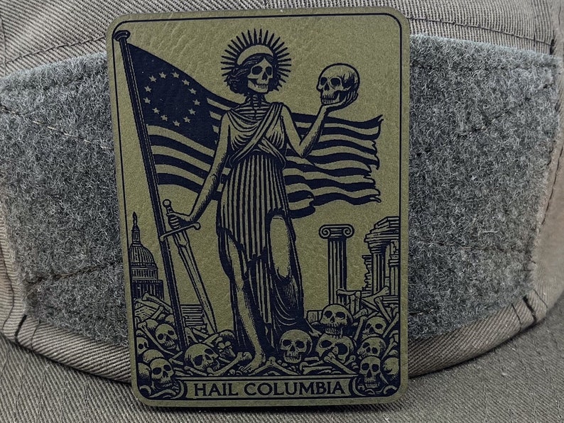 Peut inclure: Une illustration en noir et blanc d'une figure squelettique tenant un cr&acirc;ne et une &eacute;p&eacute;e, debout devant un drapeau am&eacute;ricain en lambeaux. La figure est entour&eacute;e de cr&acirc;nes et d'os. Le texte "HAIL COLUMBIA" est imprim&eacute; en bas de l'image.