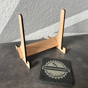 May include: A wooden easel stand with a black slate coaster featuring the text "KUNSTHANDWERK BY ANJA".