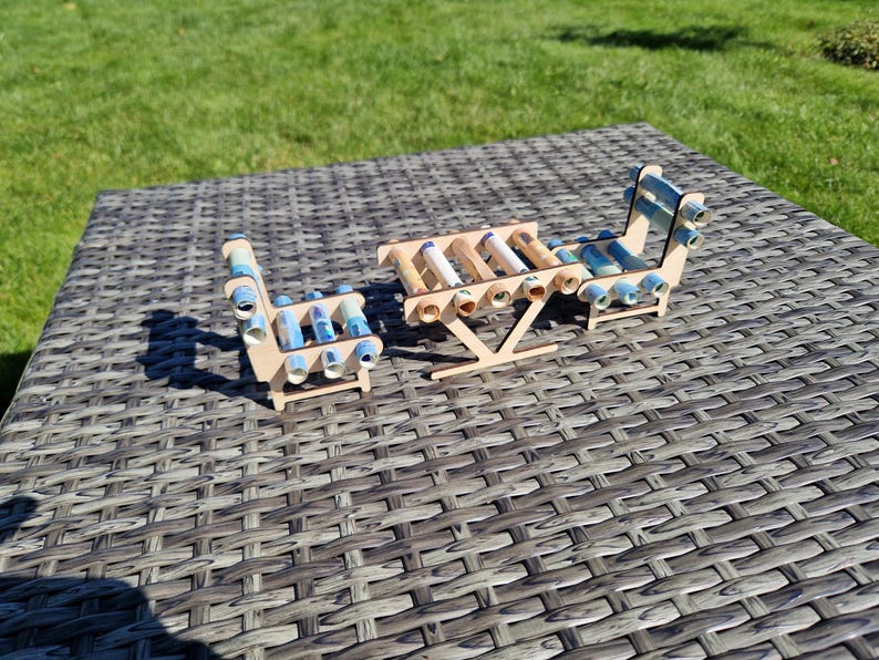 May include: A miniature furniture set consisting of a table and two chairs constructed from light-colored wood. The seats and tabletop are formed by multiple rolled-up paper currency bills in shades of blue, green, and white, secured within the frames.