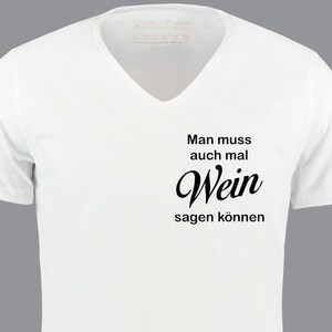 Könnte beinhalten: Weißes V-Ausschnitt-T-Shirt mit dem deutschen Satz "Man muss auch mal Wein sagen können" in Schwarz gedruckt. Das Shirt hat kurze Ärmel und einen lässigen Stil.