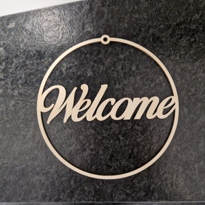 Könnte beinhalten: Ein rundes Willkommensschild aus Holz mit dem Wort "Welcome" in kursivschrift.