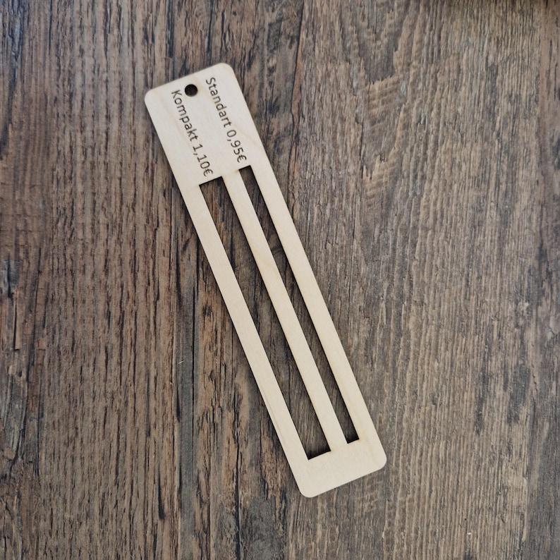 Pu&ograve; includere: Un righello di legno con due fessure per misurare. Il righello ha il testo "Standard 0.95&euro;" e "Kompakt 1.10&euro;" stampato su di esso.