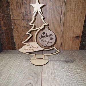 Könnte beinhalten: Ein Weihnachtsbaumschmuck aus Holz mit einem Stern oben und einer runden Kugel mit der Aufschrift "Jochen 1939-2016" mit Sternen und einem Herz. Auf dem Sockel steht "In Loving Memory".