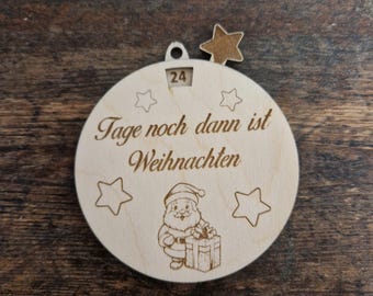 May include: A wooden Christmas ornament with the text "Tage noch dann ist Weihnachten" and a Santa Claus illustration. The ornament has a star-shaped cutout and a small window displaying the number 24. The ornament is round with star-shaped outlines.