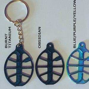 Può includere: Cinque diverse varianti di colore di un portachiavi a forma di pallacanestro. I portachiavi sono in metallo e hanno una finitura lucida. I colori sono titanio bruciato, ossidiana, blu/viola/giallo, oro/rame/nero e oro/verde/rosa-rosso.
