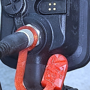 May include: A red plastic hook attached to a black metal object. The hook is shaped like a U and has a textured surface.