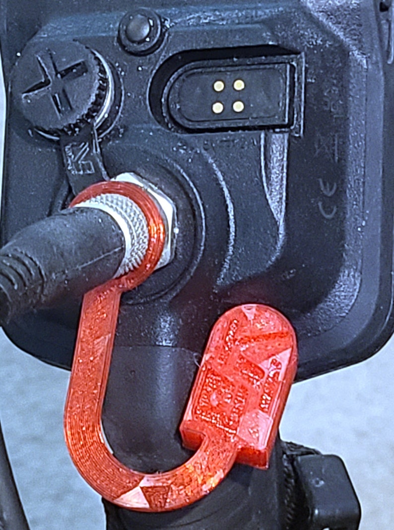 May include: A red plastic hook attached to a black metal object. The hook is shaped like a U and has a textured surface.