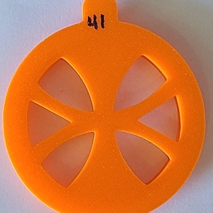 Może przedstawiać: Pomarańczowa ozdoba z tworzywa sztucznego z wyciętym wzorem przypominającym koło z czterema szprychami. Ozdoba jest oznaczona numerem "41".