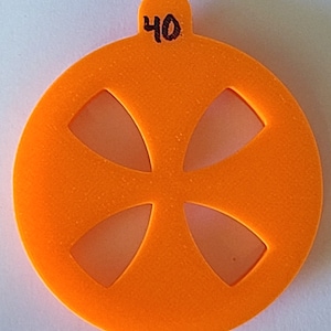 Pode incluir: Estêncil de plástico laranja com um design de estrela de quatro pontas e o número 40 escrito no topo.