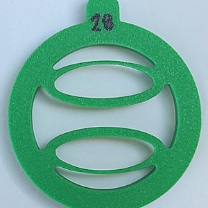 May include: Green Christmas ornament with a number 28 on the top. The ornament has a circular shape with a cut-out design of a circle with two horizontal lines.