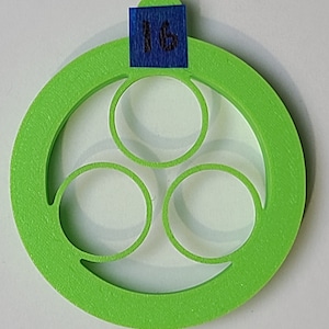May include: A bright green, circular object with three interior circles and a small tab at the top. A blue square with the number "16" is affixed to the tab. The object has a textured surface and is set against a white background.