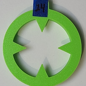 Pode incluir: Um cortador de biscoitos de plástico verde brilhante em forma de estrela de quatro pontas com um furo no centro. O cortador tem uma superfície texturizada e é etiquetado com o número "34".