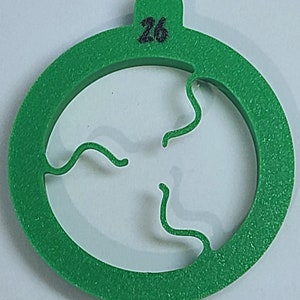 May include: Green plastic cookie cutter shaped like a circle with a three-leaf clover design cut out. The cutter is labelled with the number "26".
