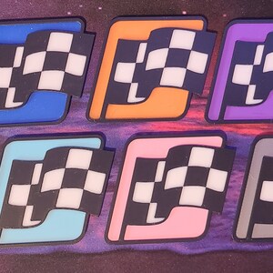 May include: Ten checkered flags in different colours, including red, blue, green, light blue, pink, grey, orange, purple, yellow, and lime green. Each flag has a white checkered pattern and a black 'L' in the corner.