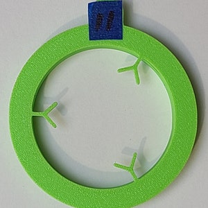 May include: A green plastic ring with three Y-shaped cutouts. The ring has a rough texture and is approximately 4 inches in diameter.