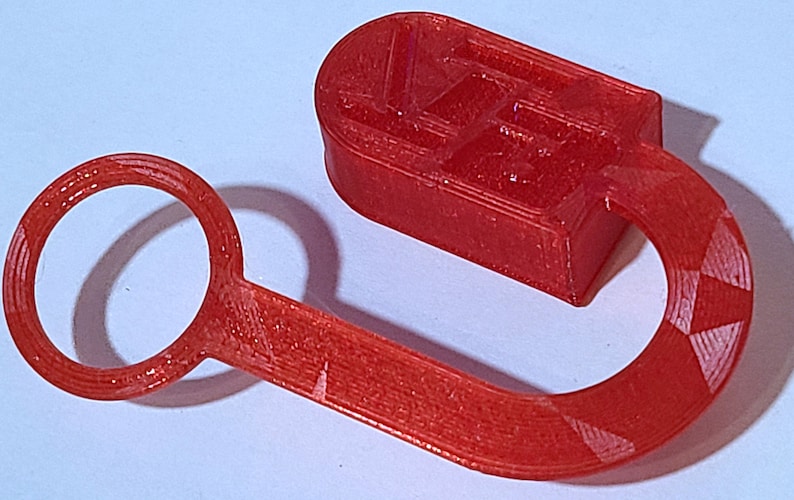 May include: A red 3D printed plastic hook with a ring on one end and a rectangular block on the other end. The block has a textured surface with a pattern.