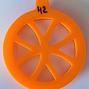 Pode incluir: Cortador de biscoitos de plástico laranja em forma de roda com seis raios. O cortador tem um pequeno laço na parte superior e o número "42" escrito nele.