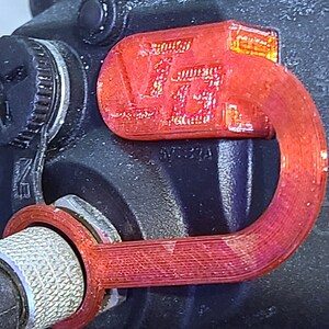 May include: A red 3D printed loop with the text "SVT32A" printed on it. The loop is attached to a black object with a silver knob.