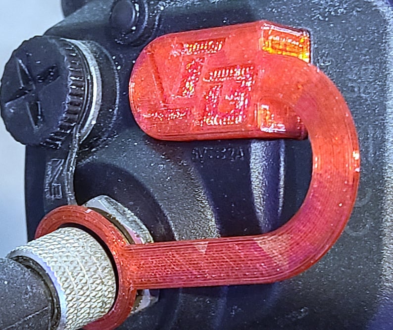 May include: A red 3D printed loop with the text "SVT32A" printed on it. The loop is attached to a black object with a silver knob.