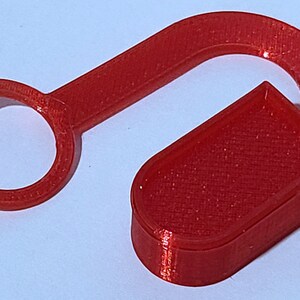 May include: A red plastic hook with a circular opening at one end and a rectangular shape at the other end.
