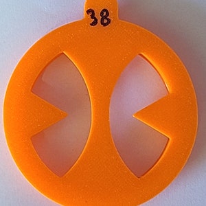 Pode incluir: Círculo de plástico laranja com o número 38 no topo e duas formas recortadas no meio. As formas são como dois triângulos com as pontas voltadas uma para a outra.