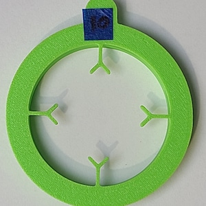 May include: A bright green plastic ring with four Y-shaped cutouts. The ring has a blue sticker on the top with the number "10" written on it.