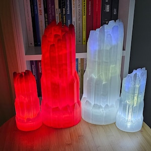 Puede incluir: Tres lámparas de cristal, una roja y dos blancas, con un diseño texturizado y facetado. Las lámparas están encendidas y proyectan un brillo cálido.