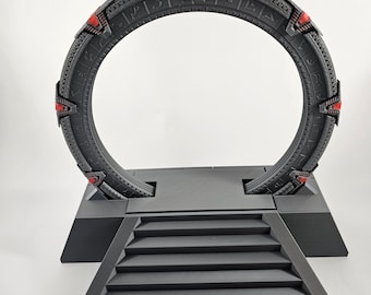 Può includere: Un modello stampato in 3D di una Stargate, un dispositivo immaginario utilizzato per i viaggi interstellari. La Stargate è nera con accenti rossi ed è montata su una base nera con gradini che conducono ad essa.