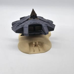 May include: A 3D printed model of a futuristic spaceship hovering over a sand dune with a pyramid structure at the base.