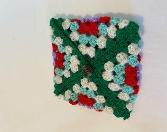 May include: A multi-coloured crocheted square with a button fastening. The granny square design incorporates green, red, light blue, white, and purple. The button is a dark, neutral shade.