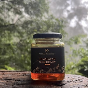 Könnte beinhalten: Ein Glas Honig aus dem Himalaya Sidr mit einem schwarzen Etikett mit der Aufschrift "Himalayan Sidr Honey Wild" und einer Berg-Grafik. Das Glas enthält 250g Honig und steht vor einem verschwommenen grünen Hintergrund.